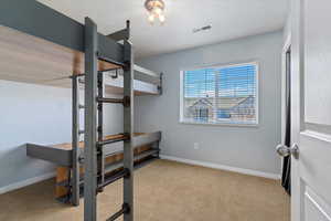 Bedroom featuring light carpet, baseboards, visible vents, and a textured ceiling