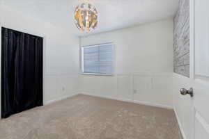 Spare room with wainscoting, a textured ceiling, and light colored carpet