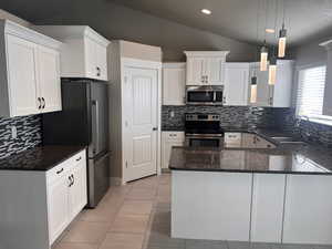 Kitchen featuring stainless steel appliances, lofted ceiling, white cabinets, sink, and pendant lighting