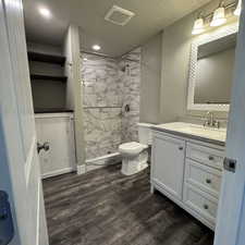 Bathroom with vanity, toilet, a textured ceiling, tiled shower, and wood-type flooring