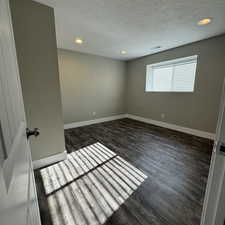 Empty room with dark hardwood / wood-style floors and a textured ceiling