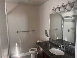 Bathroom featuring walk in shower, vanity, a textured ceiling, tile patterned flooring, and toilet