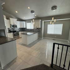 Kitchen with appliances with stainless steel finishes, vaulted ceiling, white cabinetry, and pendant lighting