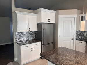 Kitchen featuring white cabinets, tasteful backsplash, light tile patterned flooring, pendant lighting, and stainless steel fridge