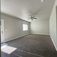 Carpeted empty room featuring a textured ceiling and ceiling fan