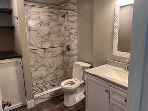 Bathroom with toilet, hardwood / wood-style floors, vanity, and a tile shower