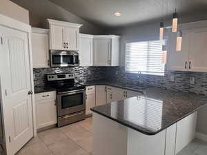 Kitchen featuring kitchen peninsula, sink, white cabinetry, appliances with stainless steel finishes, and decorative light fixtures