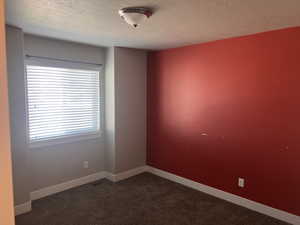 Unfurnished room with a textured ceiling and dark carpet