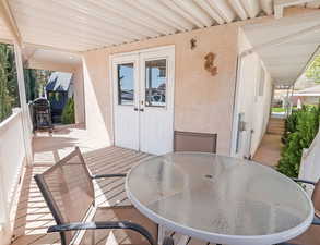 Exterior deck space with outdoor dining area with retractable sunshades, French doors to workshop/storage. and sidewalk walkway around entire house with beautiful landscaping