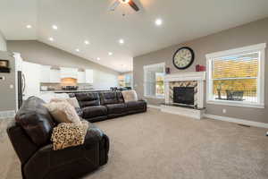 Carpeted living room with ceiling fan, a tile fireplace, and vaulted ceiling