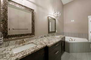 Bathroom with a notable chandelier, vanity, tile patterned floors, and tiled tub