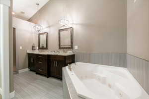 Bathroom with tile patterned floors, vaulted ceiling, an inviting chandelier, vanity, and a relaxing tiled tub