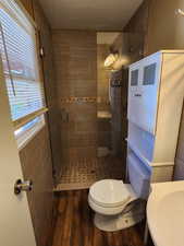 Bathroom featuring hardwood / wood-style flooring, a shower with door, toilet, and tile walls