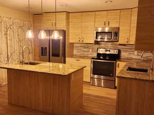 Kitchen featuring appliances with stainless steel finishes, sink, decorative light fixtures, and light stone countertops