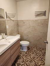 Bathroom with tile patterned floors, vanity, toilet, and tile walls