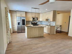 Kitchen with appliances with stainless steel finishes, light brown cabinetry, hanging light fixtures, sink, and a kitchen island with sink