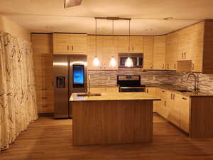 Kitchen featuring sink, a kitchen island with sink, light wood-type flooring, appliances with stainless steel finishes, and decorative light fixtures