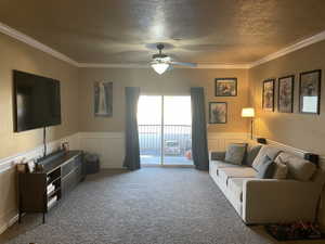 Carpeted living room with ceiling fan, a textured ceiling, and ornamental molding