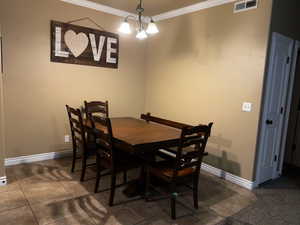 Dining room with dark tile patterned flooring, a notable chandelier, and ornamental molding