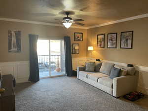 Carpeted living room featuring a textured ceiling, ceiling fan, and crown molding