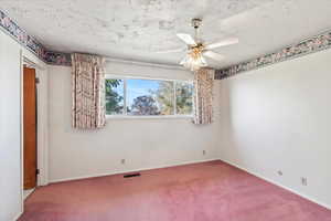 Carpeted empty room featuring a textured ceiling and ceiling fan