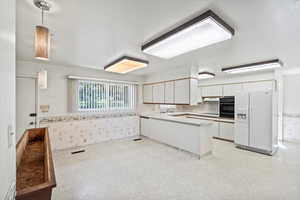 Kitchen with white cabinets, kitchen peninsula, black appliances, extractor fan, and decorative light fixtures