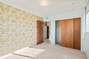 Unfurnished bedroom featuring light colored carpet, a textured ceiling, and a closet