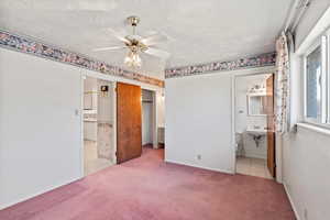 Unfurnished bedroom with a textured ceiling, light colored carpet, ceiling fan, and ensuite bathroom