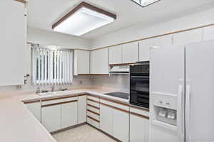 Kitchen with white cabinets, sink, black appliances, and range hood