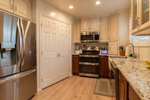 Kitchen with cream cabinets, light stone counters, light hardwood / wood-style flooring, sink, and appliances with stainless steel finishes