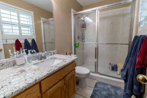 Bathroom featuring toilet, vanity, tile patterned flooring, and a shower with door