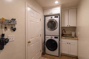 Washroom with cabinets, stacked washer and dryer, and sink