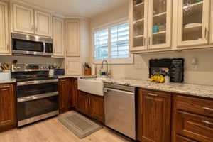 Kitchen featuring light stone counters, appliances with stainless steel finishes, sink, light hardwood / wood-style floors, and cream cabinetry