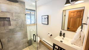 Bathroom featuring toilet, tile patterned flooring, tiled shower, and baseboard heating