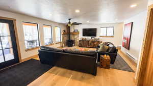 Living room with ceiling fan, a textured ceiling, a wood stove, light hardwood / wood-style flooring, and a baseboard radiator