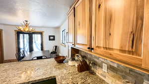 Kitchen with an inviting chandelier, a textured ceiling, backsplash, and light stone counters