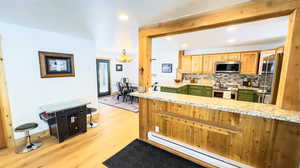 Kitchen with stainless steel appliances, green cabinets, a chandelier, light hardwood / wood-style flooring, and a baseboard radiator