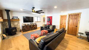 Living room with a wood stove, light hardwood / wood-style floors, a textured ceiling, and ceiling fan