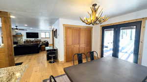 Dining room featuring ceiling fan with notable chandelier, a textured ceiling, a stone fireplace, and light wood-type flooring