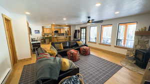 Living room featuring a textured ceiling, a wood stove, baseboard heating, ceiling fan, and light hardwood / wood-style flooring