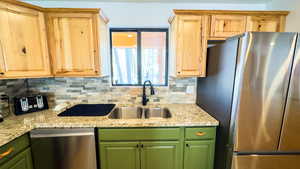 Kitchen featuring stainless steel appliances, light brown cabinetry, light stone countertops, decorative backsplash, and sink