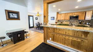 Kitchen with stainless steel appliances, light hardwood / wood-style floors, a baseboard radiator, and light stone countertops