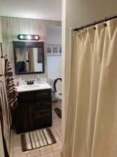 Bathroom with vanity, curtained shower, toilet, and tile patterned floors