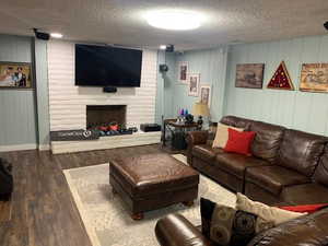 Living room featuring dark wood-type flooring, a textured ceiling, and a fireplace