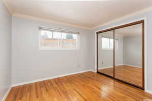 Unfurnished bedroom with multiple windows, ornamental molding, a closet, and wood-type flooring