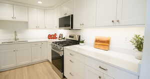 Kitchen featuring white cabinets, sink, light hardwood / wood-style flooring, and appliances with stainless steel finishes