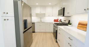 Kitchen with white cabinets, light hardwood / wood-style floors, sink, and appliances with stainless steel finishes