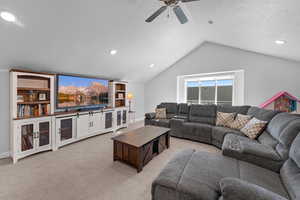 Carpeted living room featuring ceiling fan, a textured ceiling, and lofted ceiling