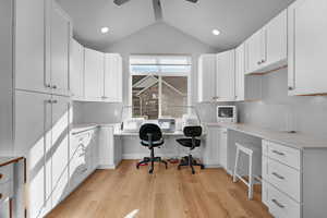 Office space featuring light hardwood / wood-style floors, lofted ceiling, built in desk, and ceiling fan