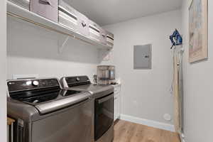 Clothes washing area with separate washer and dryer, electric panel, light hardwood / wood-style floors, and cabinets